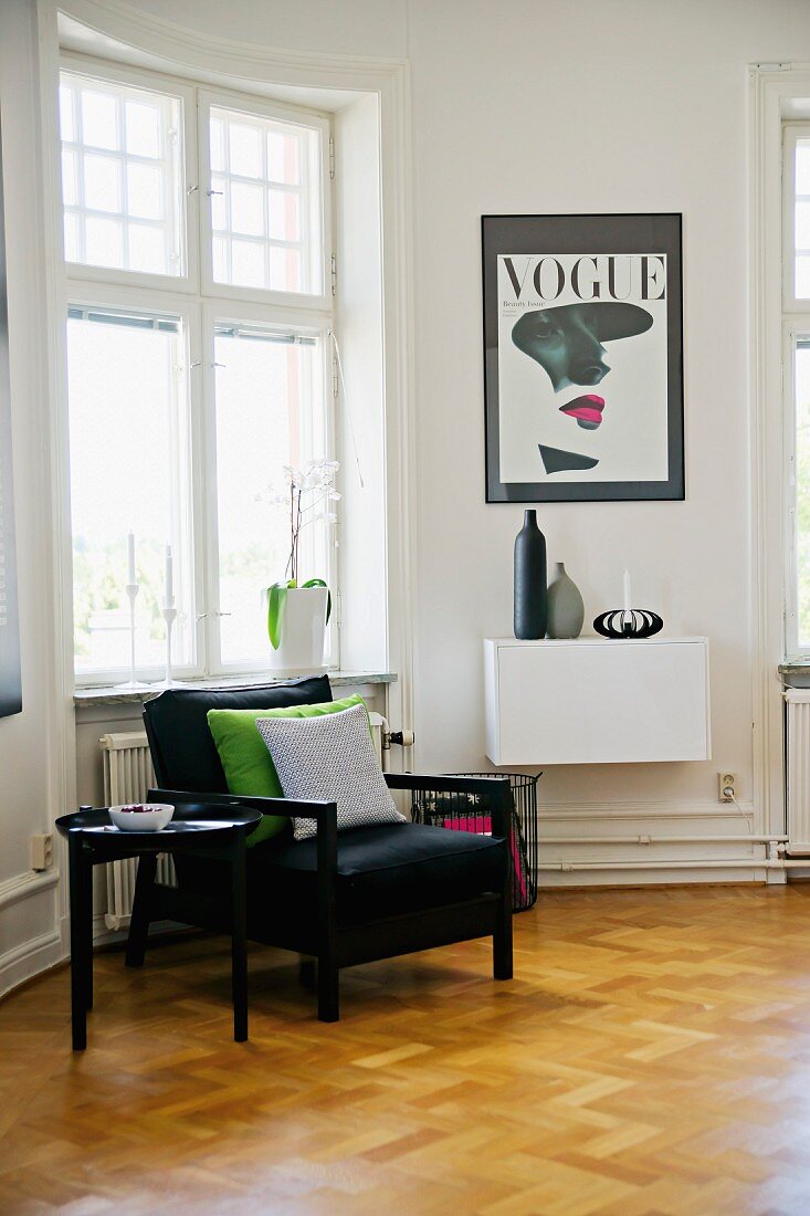 Black armchair and side table on herringbone parquet floor below window in period apartment