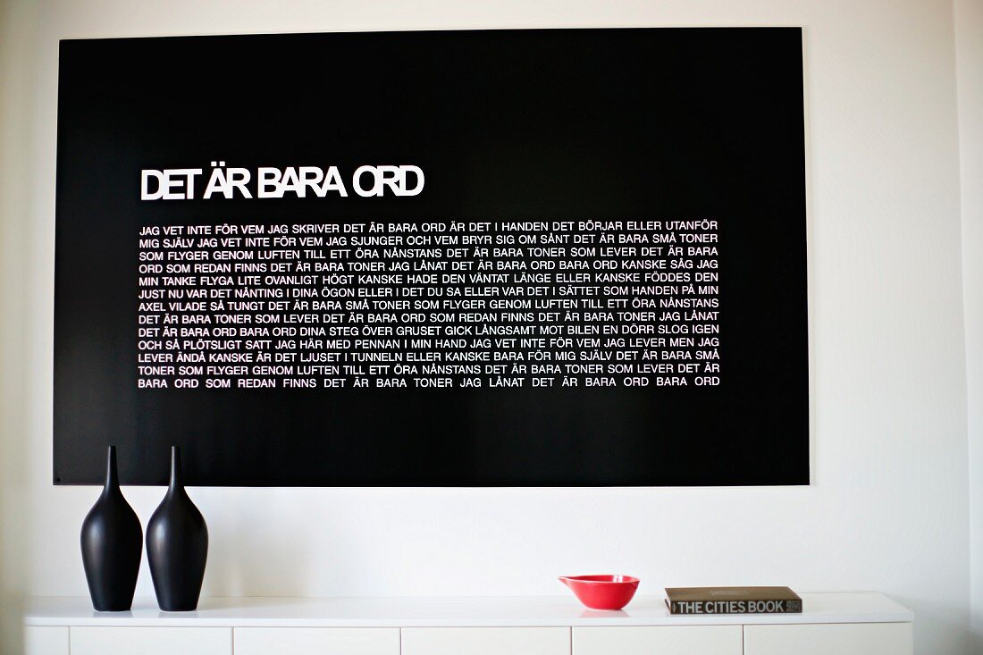 Schwarze Gefässe auf weisser Ablage, an Wand schwarze Tafel mit Text