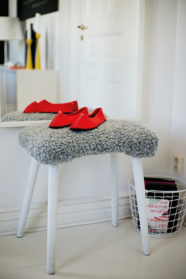 Red slippers on stool with grey, fur-like cover in front of mirror on wall