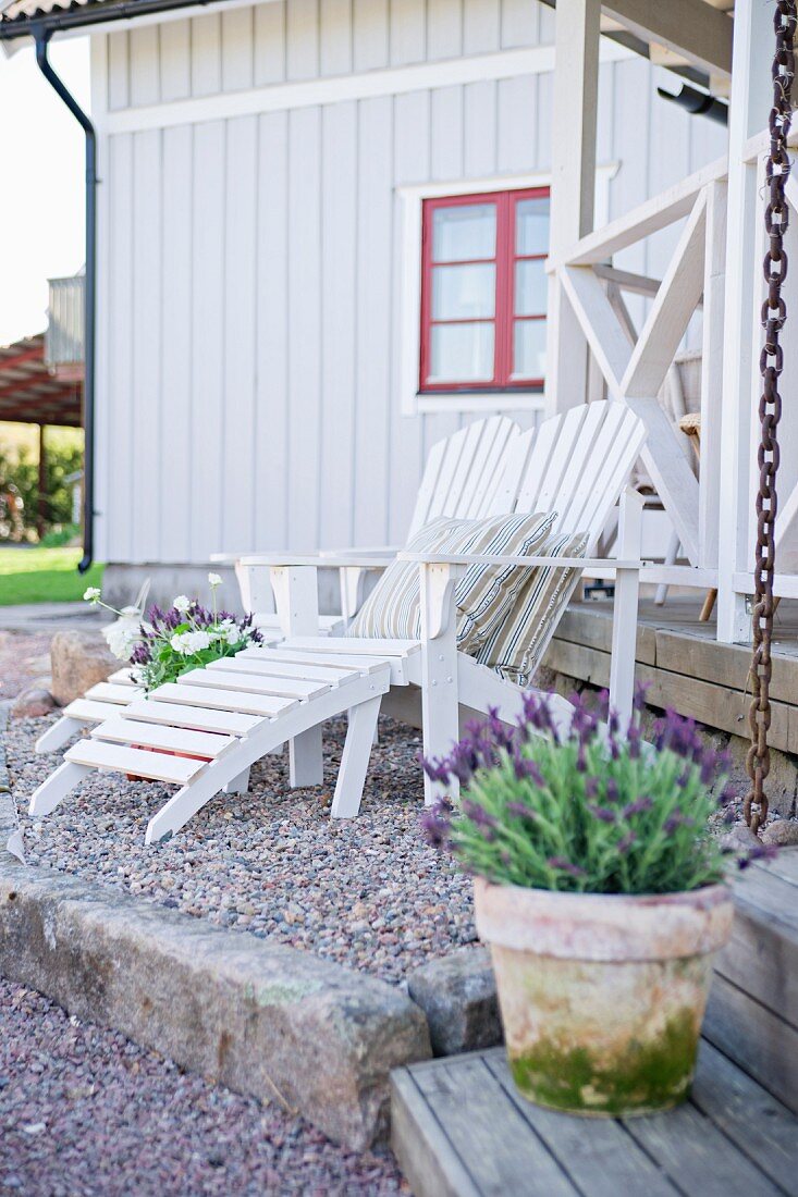 White wooden lounger on gravel terrace outside wooden house with red window