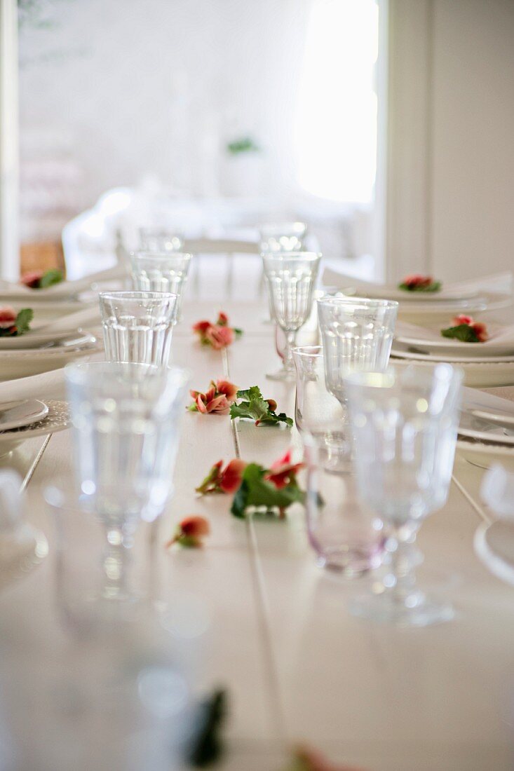 Gedeckte Tafel mit Rosenblüten zwischen den Gläsern auf weißem Esstisch