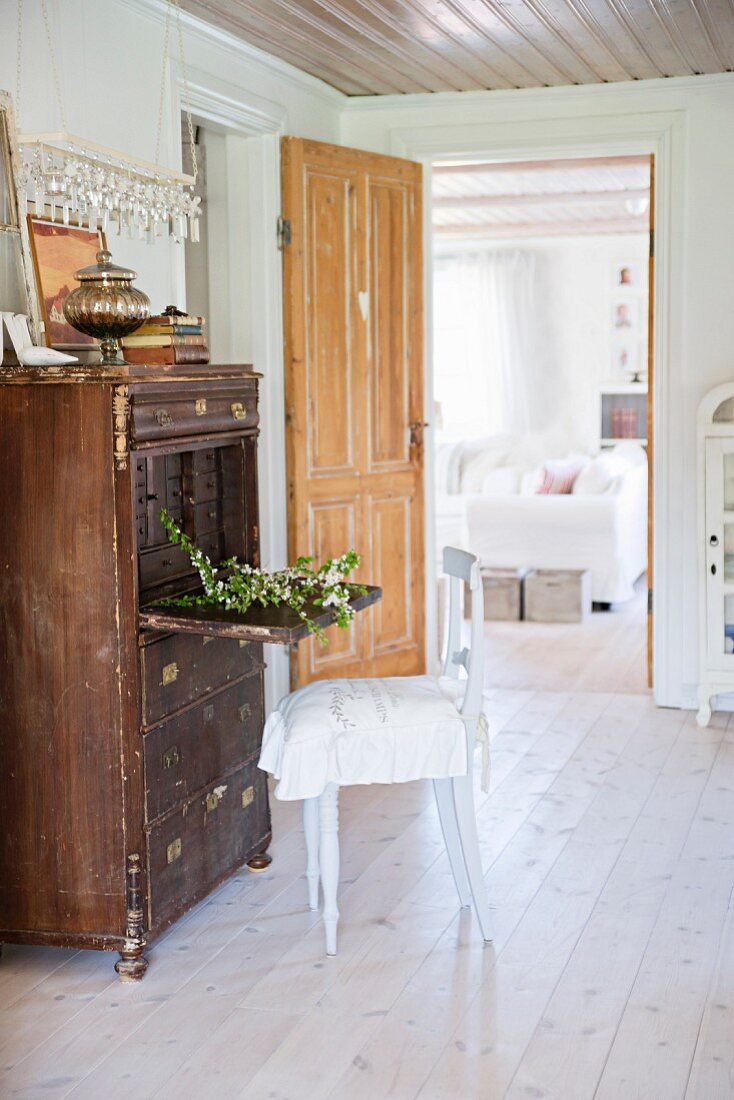 Ländlicher Stuhl vor Vintage Sekretär, im Hintergrund offene Tür und Blick ins Wohnzimmer