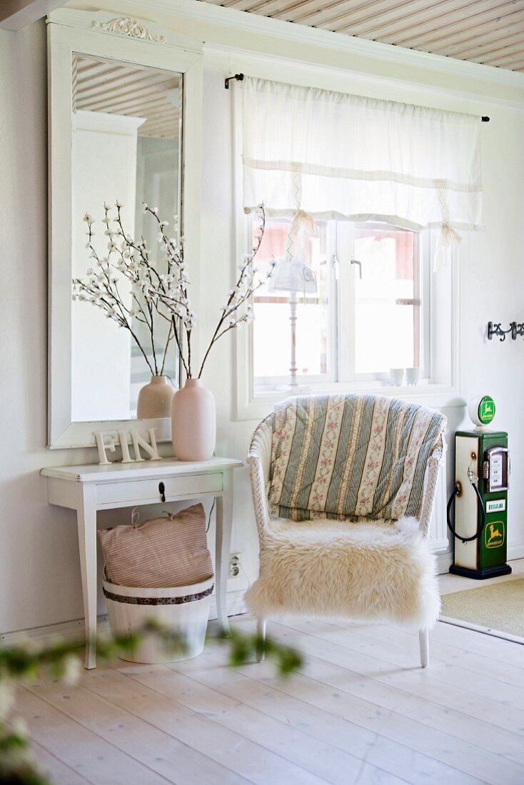 Rattansessel mit weißem Fell und Wandtisch vor gerahmtem Spiegel an Wand in ländlichem Wohnraum