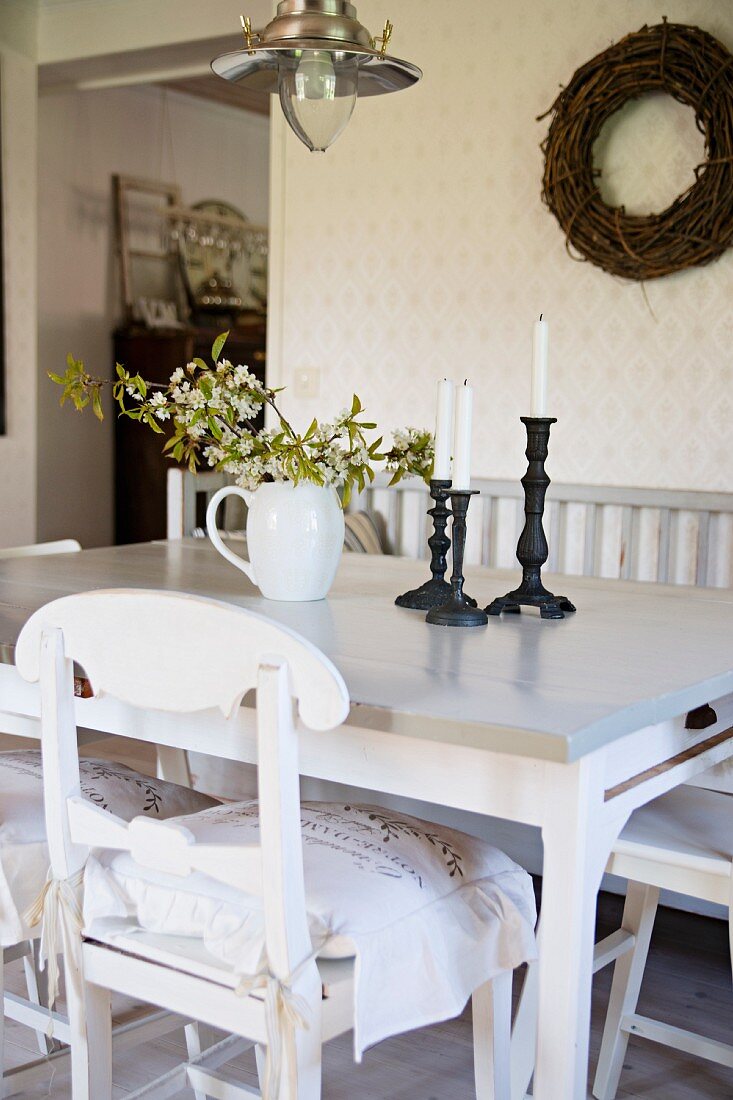 Weisser Küchenstuhl mit geschwungenem Rückenlehnenteil vor Esstisch, an Wand Kranz aus Weidenzweigen in ländlichem Ambiente