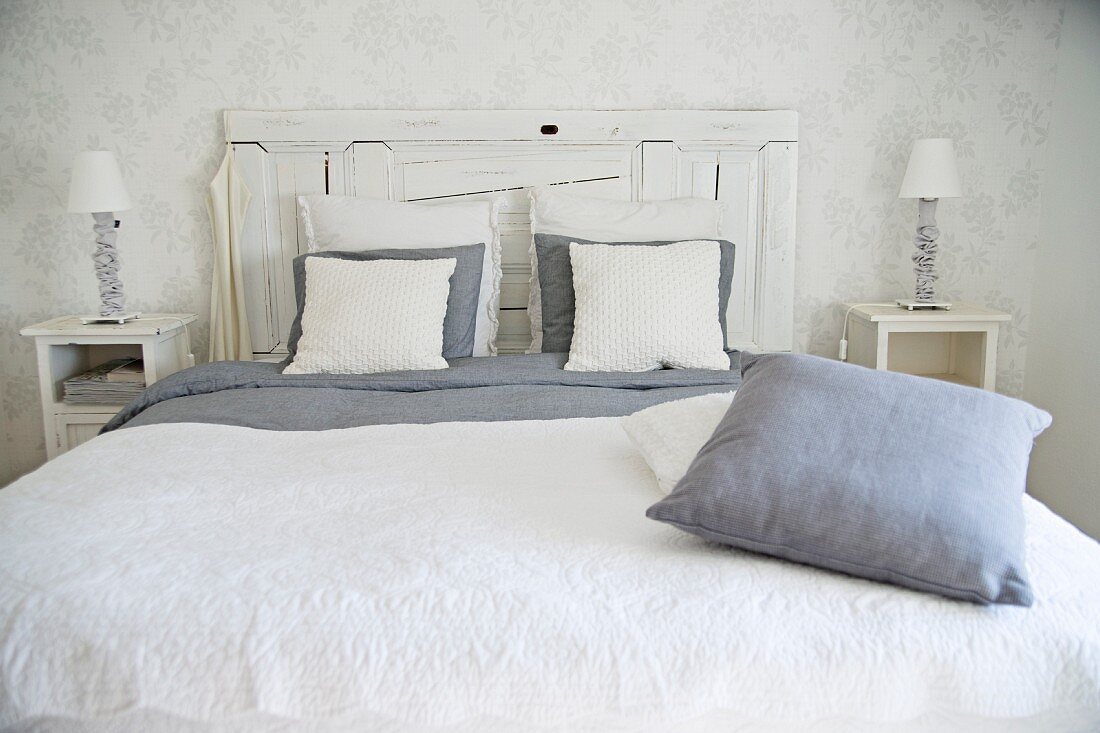 Doppelbett mit Kopfteil aus weisslackiertem Holz, weisses Plaid und Kissen in grauen und weissen Farbtönen