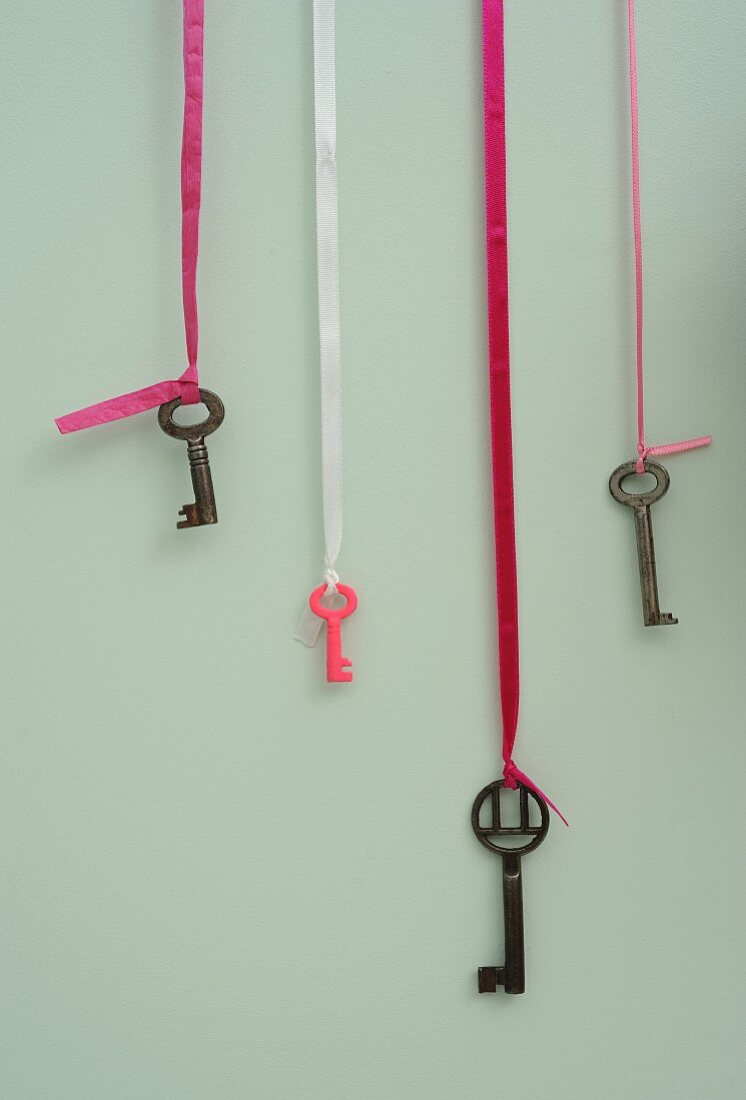 Old keys, one painted pink hanging from gift ribbon on pastel-green wall