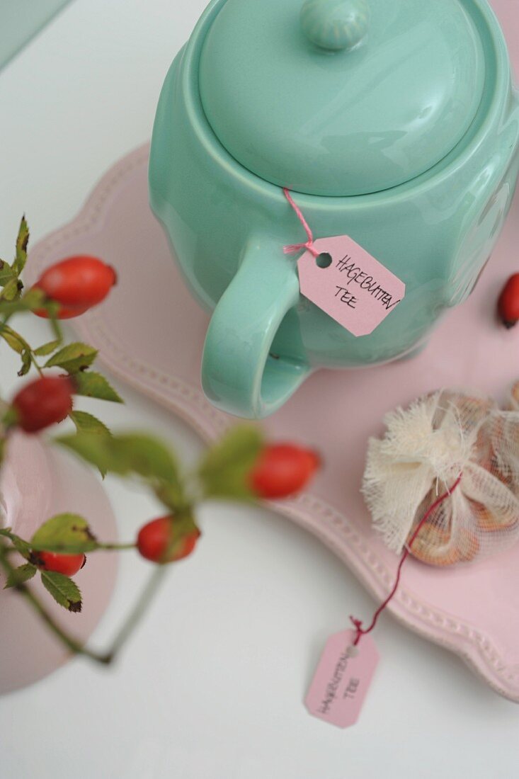 Türkisgrüne Teekanne mit Hagebuttentee, seitlich Hagebuttenzweig im Vintage Ambiente