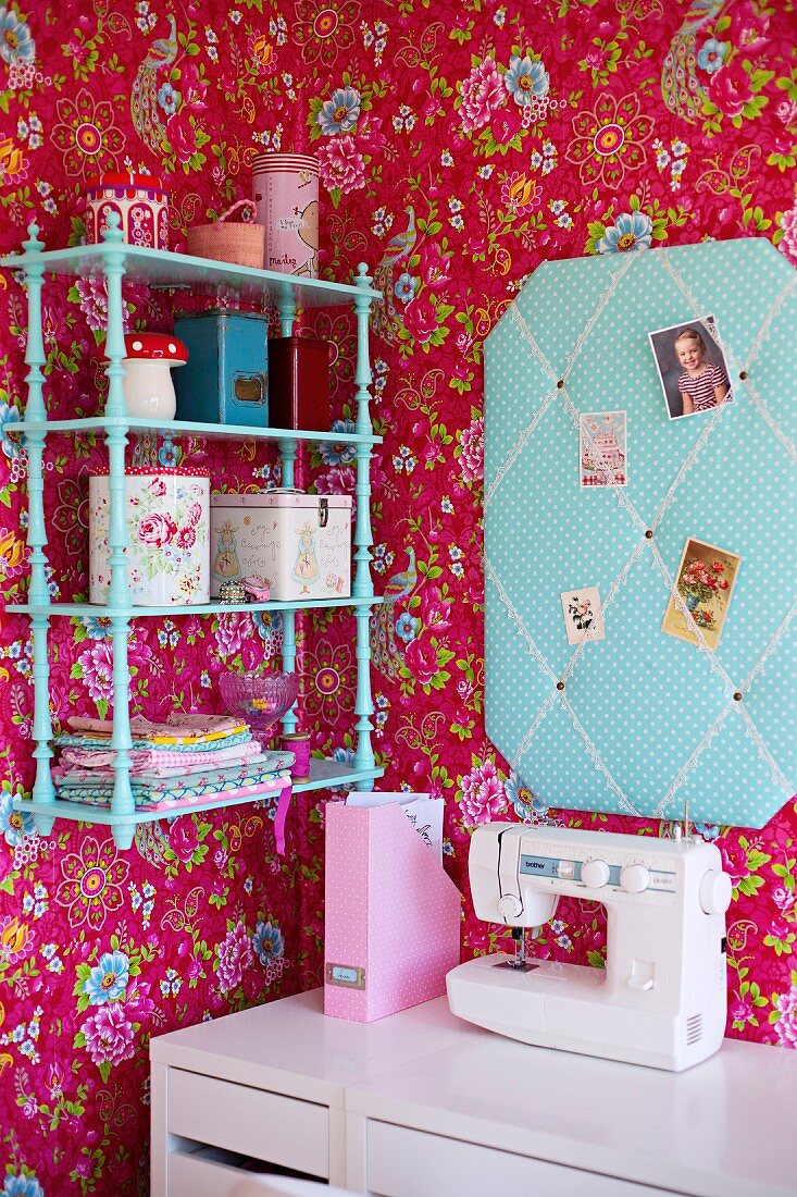 Corner of girl's bedroom with pink floral wallpaper, turquoise fabric pin board and matching wall-mounted shelves