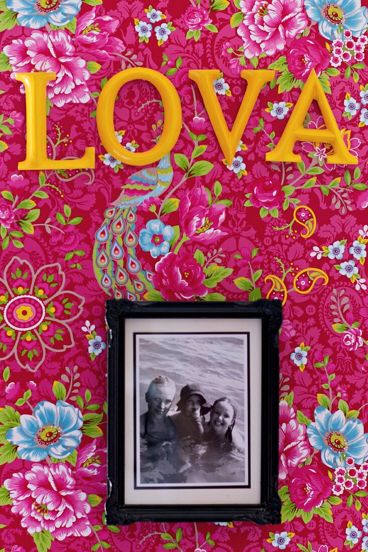 Framed family photo below yellow letters on pink, floral wallpaper