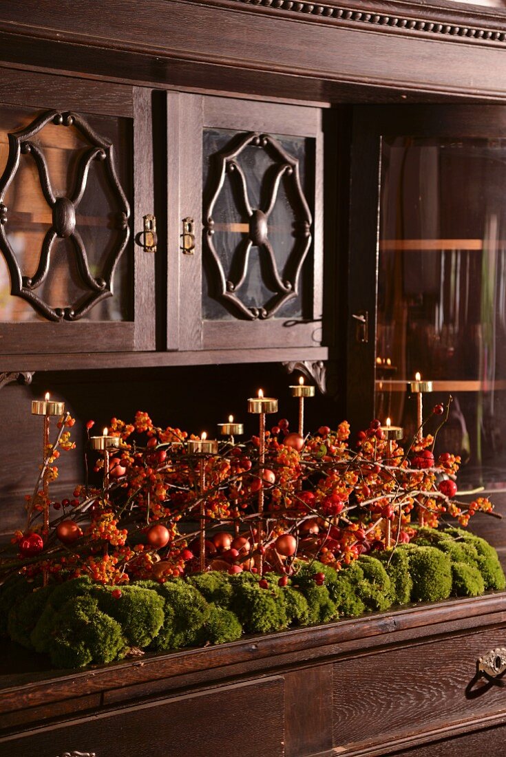Weihnachtliches Gesteck aus roten Beeren und Messing Teelichter auf Moos und Ablage eines Buffets