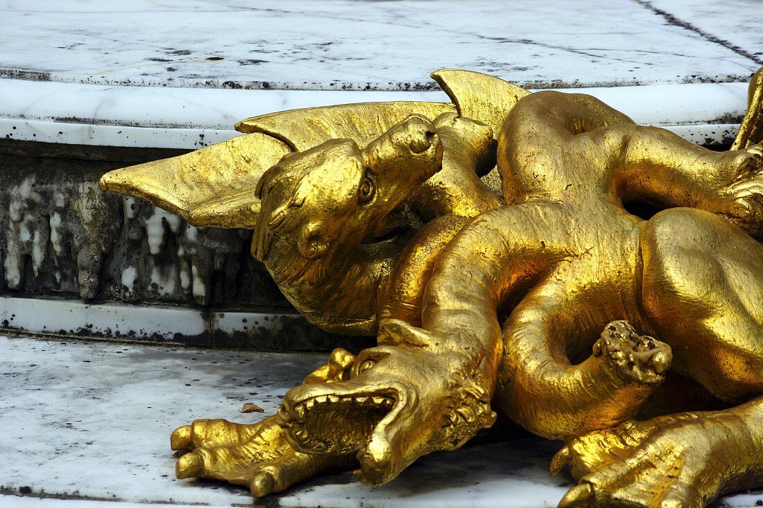 A gilded dragon statue on a stone floor in the Garden of the Palace of Versailles