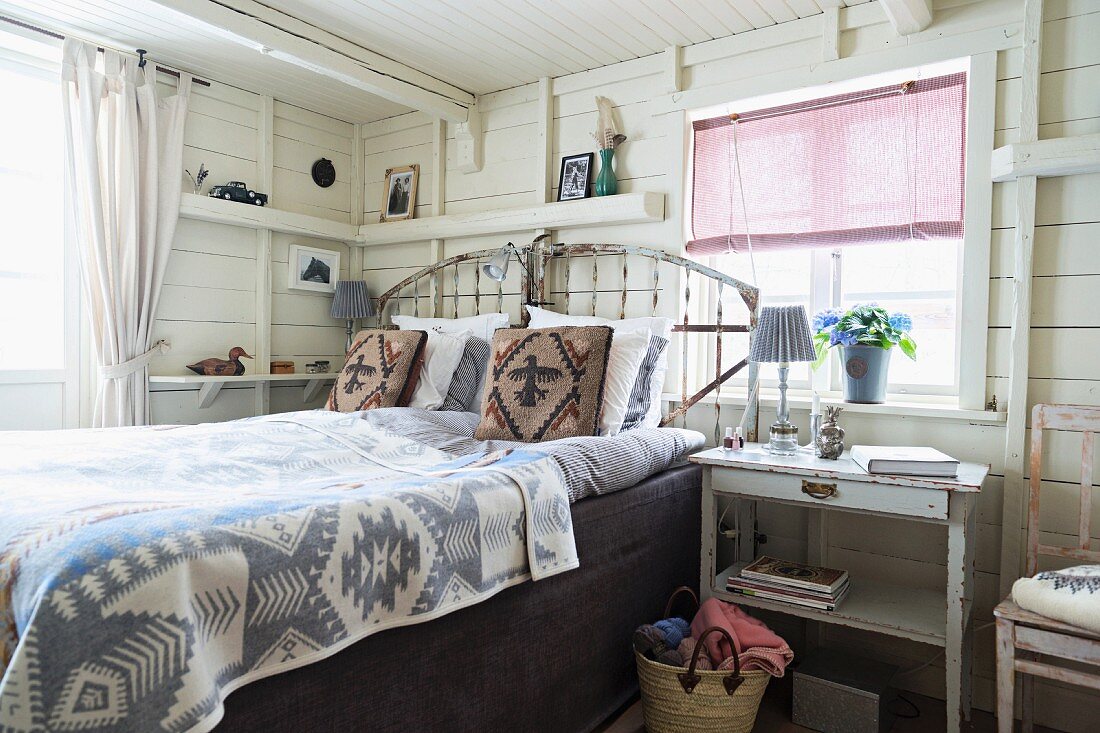 Ethnic bedspread on double bed with headboard in white, wood-clad bedroom
