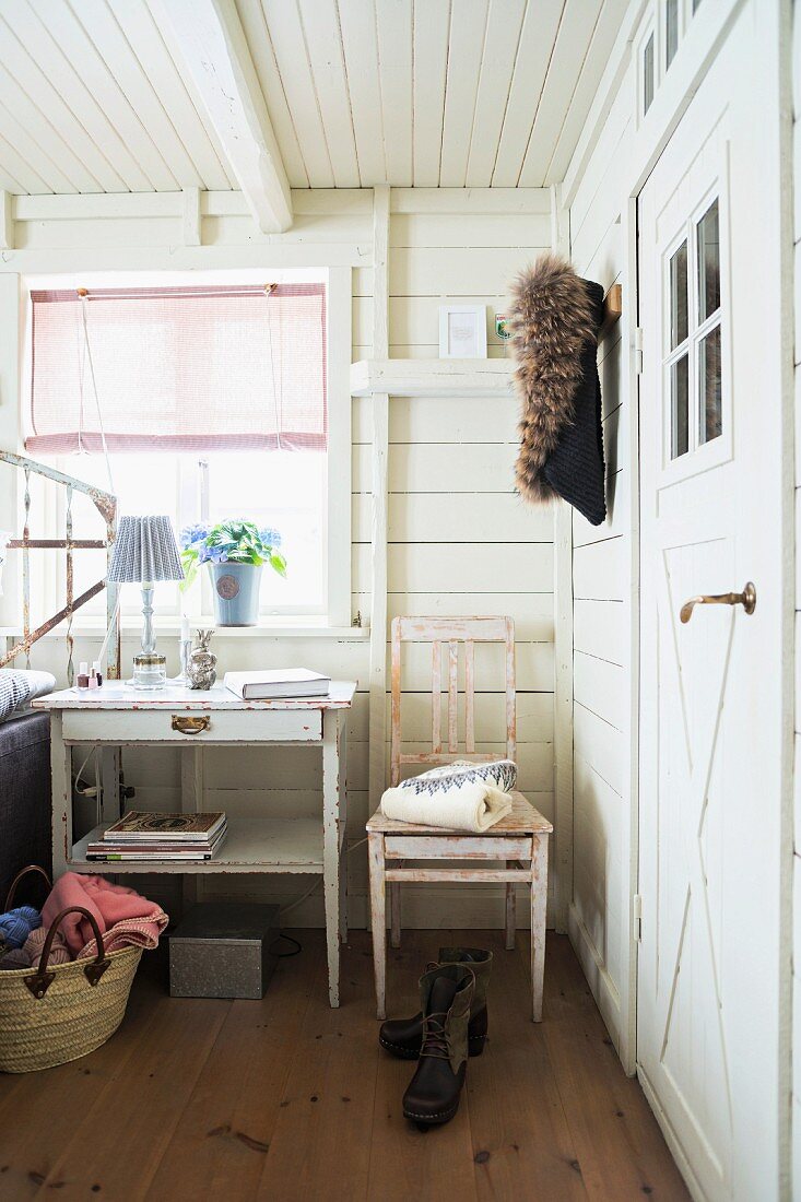 Bedside table below window and kitchen chair against white wooden wall in rustic bedroom
