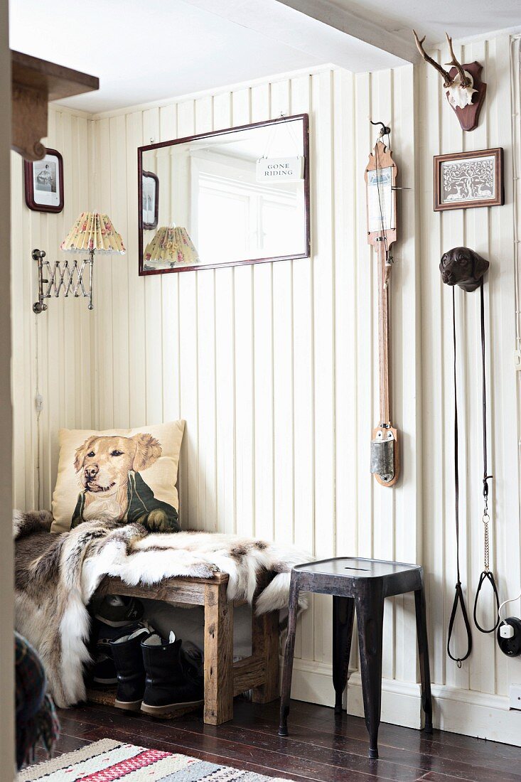 Klassiker Metallhocker neben Bank mit Tierfell und Kissen vor weisser Holzwand im Vorraum