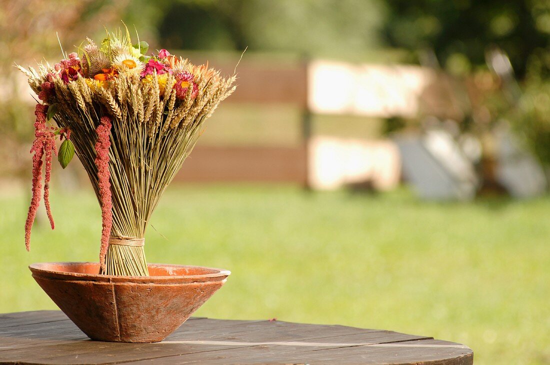 Ährenstrauss mit Blüten in Tonschale auf Gartentisch