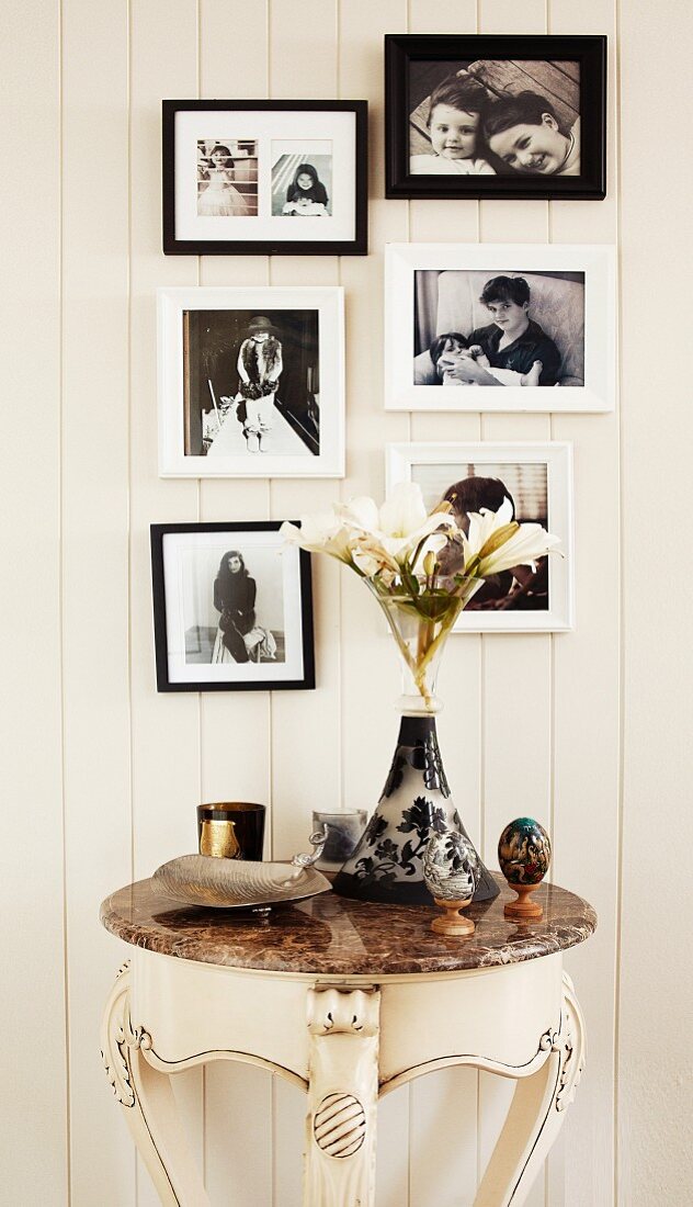 Framed black and white family photos above antique console table with marble top