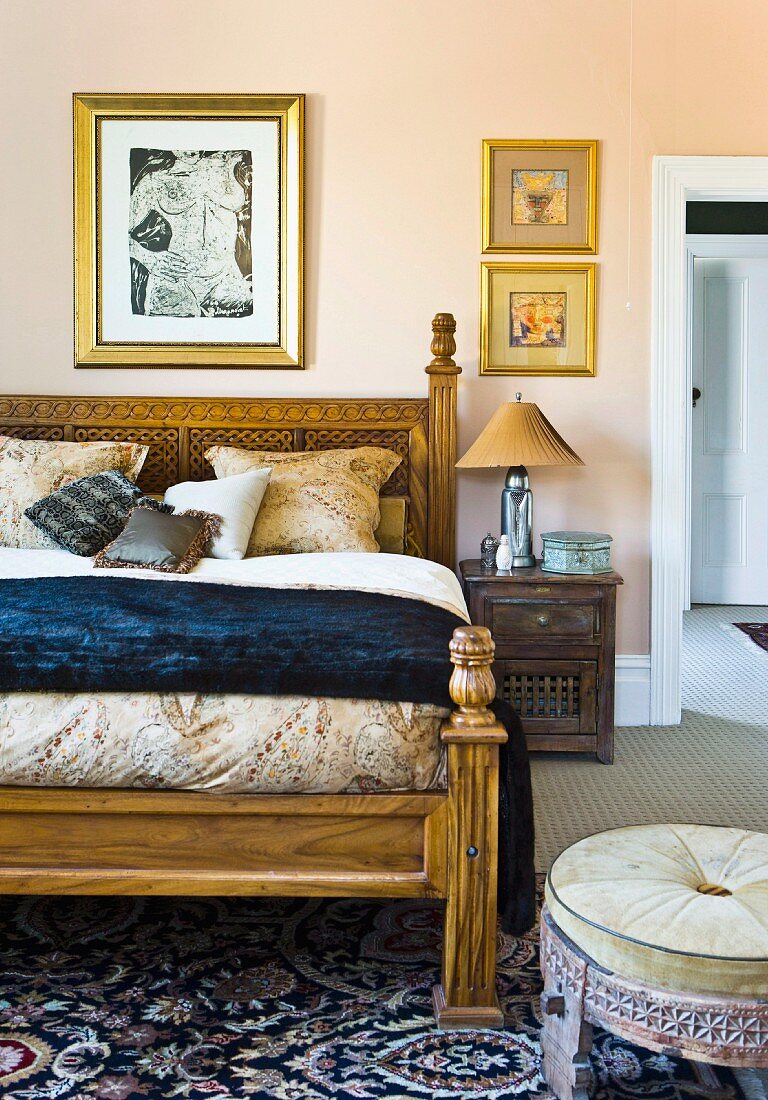 Elegantes Doppelbett mit geschnitztem Holzgestell, davor Sitzhocker in orientalischem Stil im Schlafzimmer