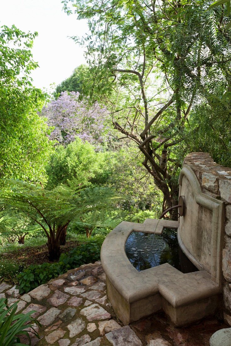 Betonbrunnen an Natursteinmauer im Waldähnlichen Garten