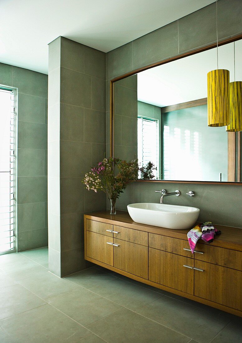Washstand with basin on wooden base unit and large mirror on grey tiled wall in modern bathroom