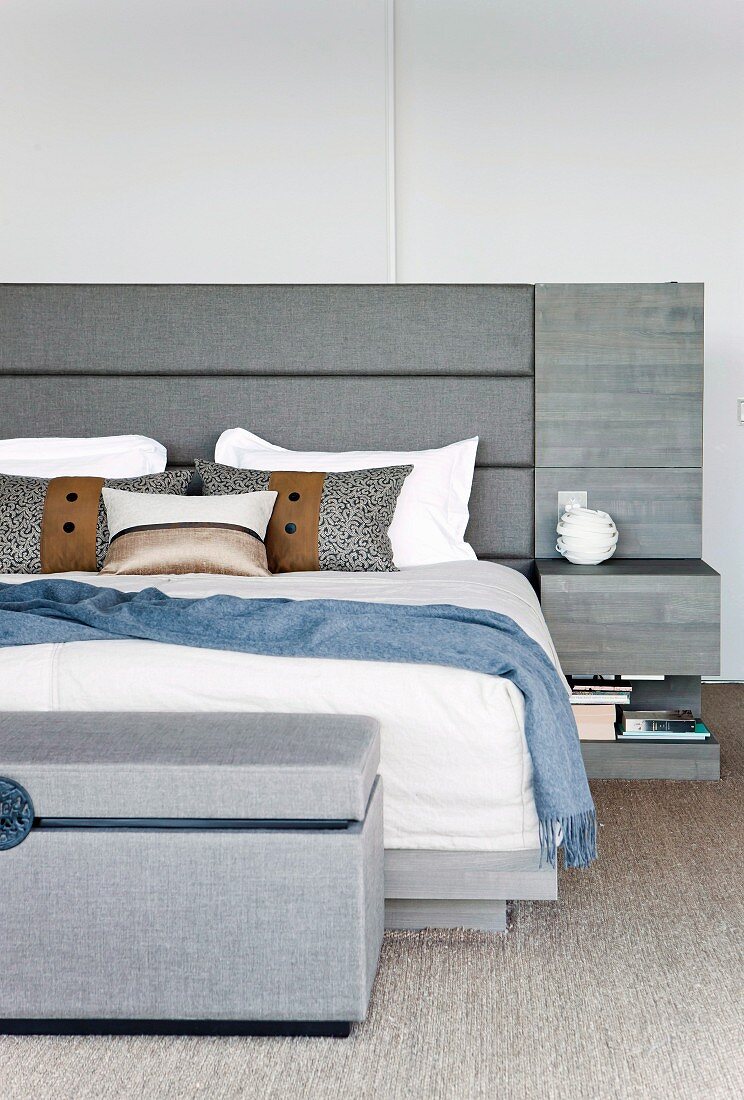 Elegantes Doppelbett mit grau gepolstertem Kopfteil, integrierten Nachtkästchen und passender Kleiderbank