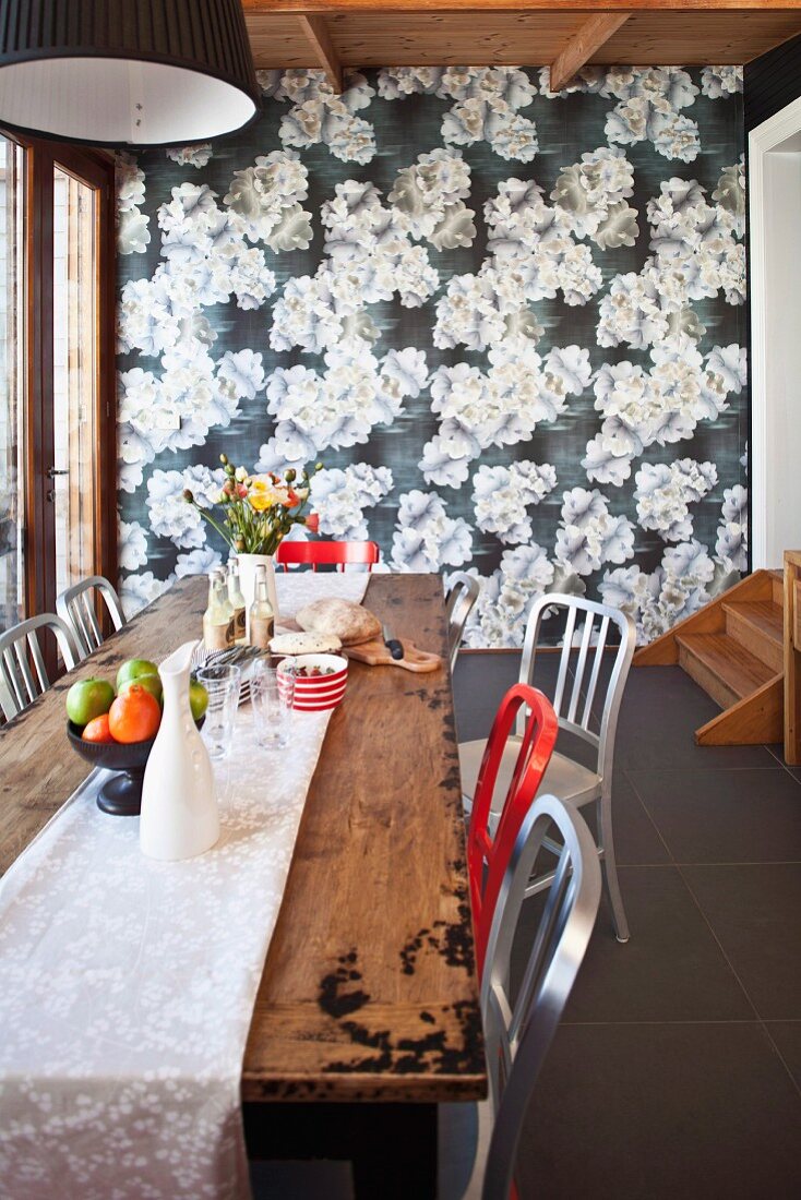 Rote und weiße Stühle an rustikalem Holztisch vor tapezierter Wand mit Blumenmuster