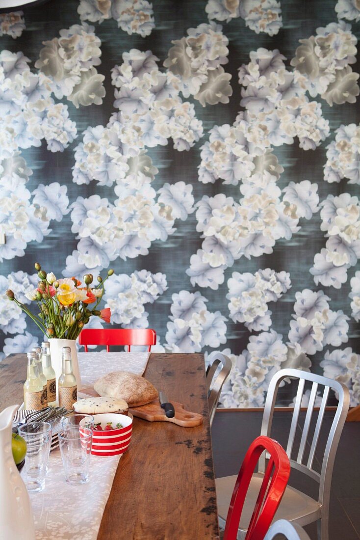 Vase of flowers on wooden table in front of wall covered in floral wallpaper