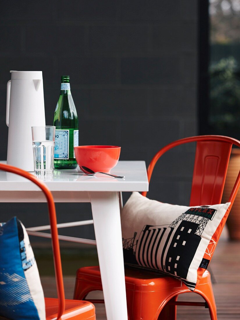 Kissen mit Kunstdrucken auf orangefarbenen Vintage Stühlen an Tisch auf der Terrasse
