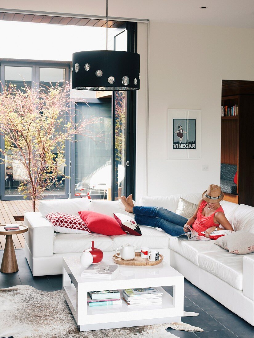 Bright living room with folding sliding doors to courtyard; young woman relaxing on corner sofa with scatter cushions