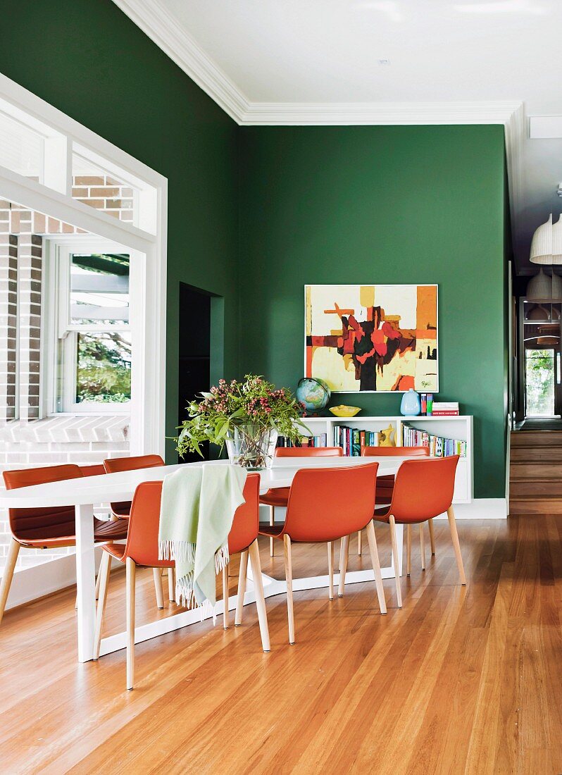 Offener Essbereich, rotbraune Schalenstühle um Tisch in Zimmerecke vor Fenster, im Hintergrund grün getönte Wand