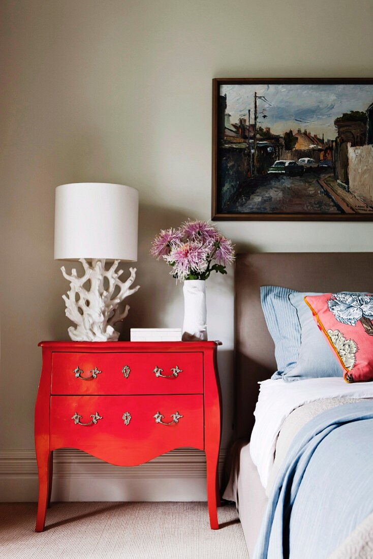Roter Vintage Sekretär mit weisser Tischleuchte neben Bett, an Wand gerahmtes Bild