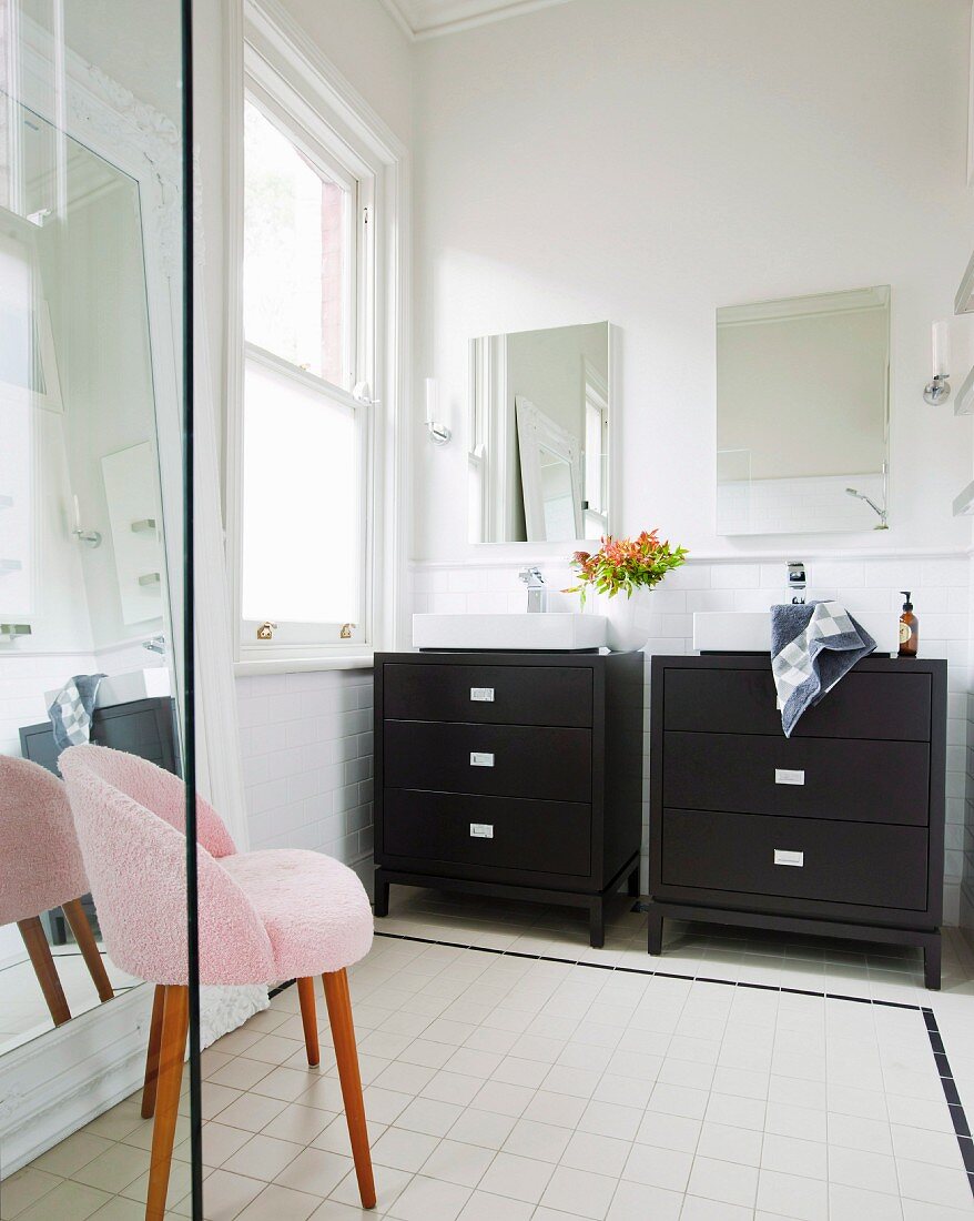 Twin washstands with black base units below mirrors and pink fifties armchair on pale tiles floor