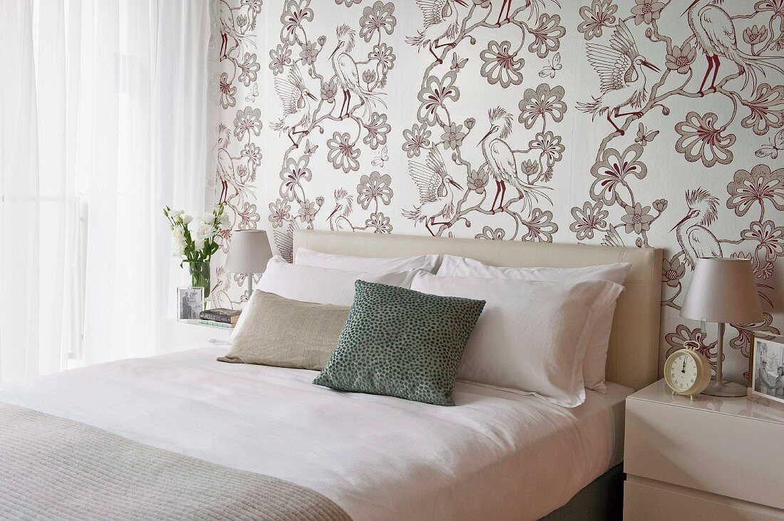Elegant, bright bedroom with bird-patterned wallpaper and scatter cushions on double bed with upholstered headboard