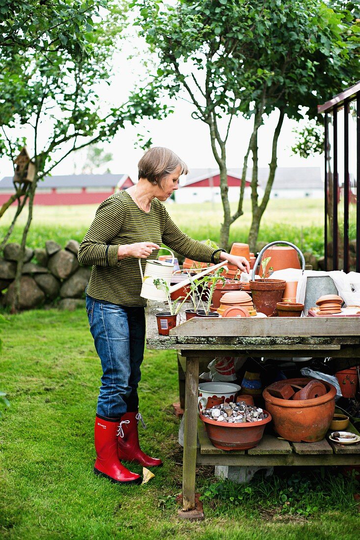 Frau bei Gartenarbeit - verschiedene Tontöpfe auf Holztisch mit Ablage im Garten