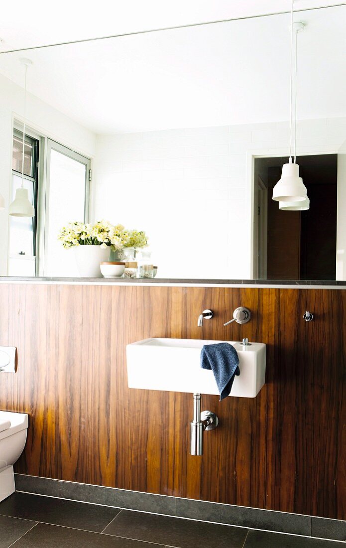 Sink and toilet against half-height wall panelled in exotic wood