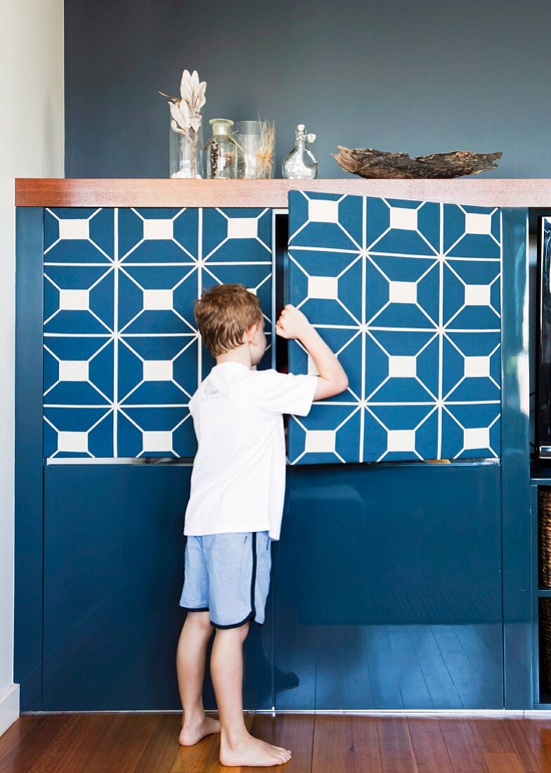 Junge beim Öffnen der Tür eines blau lackierten Schranks mit grafischer Musterung
