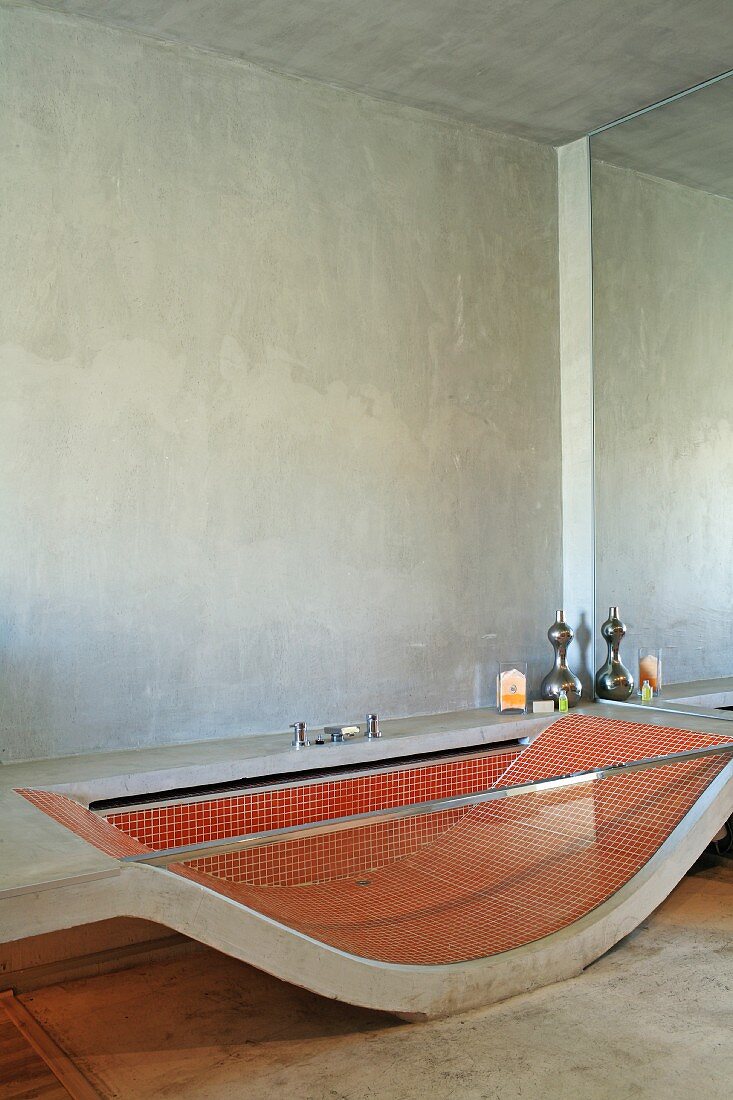 Badewanne aus gebogener Betonplatte und Seitenwand aus Glas, innenseitig rote Mosaikfliesen in minimalistischem Bad
