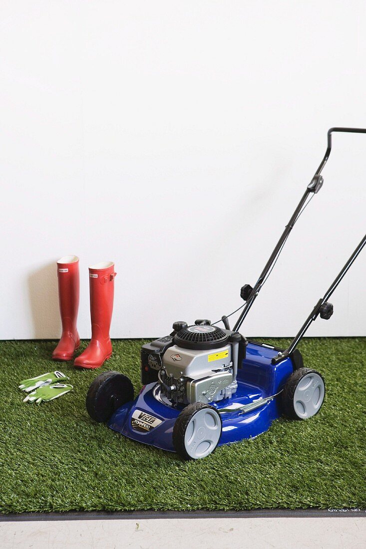 Lawn-mower and gardening equipment on artificial lawn against white wall