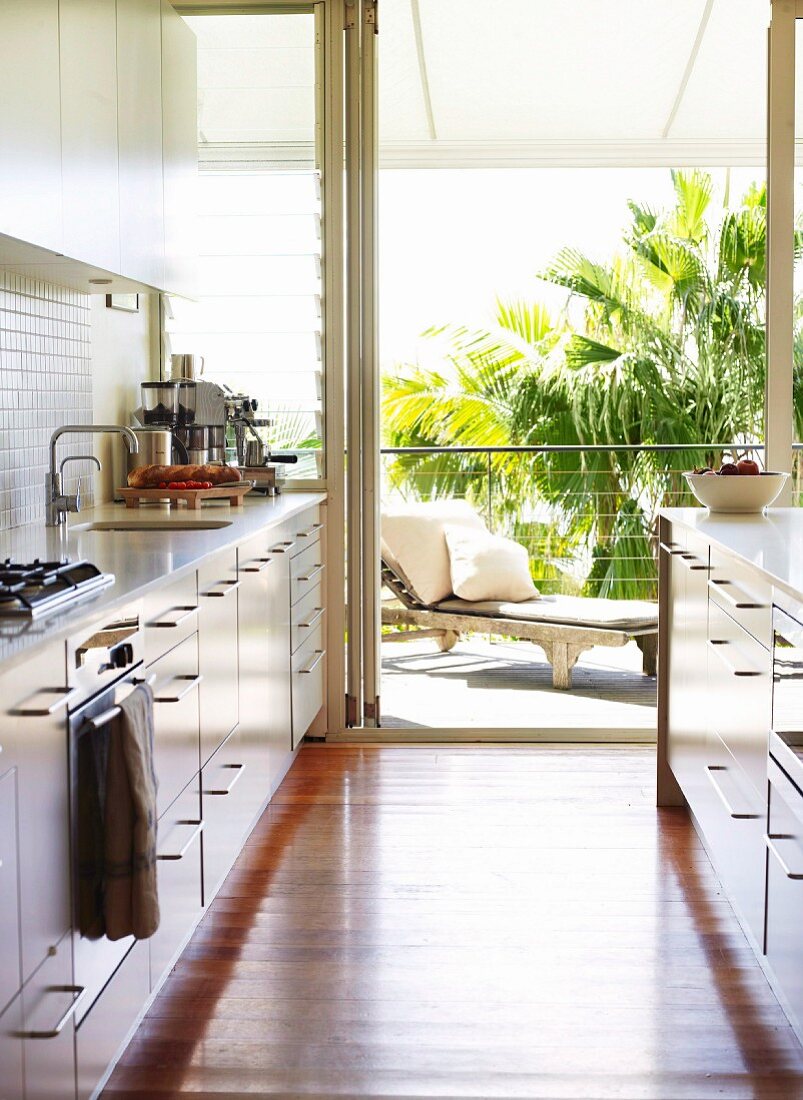 Blick von moderner Einbauküche auf Terrasse mit Sonnenliege und Palmen