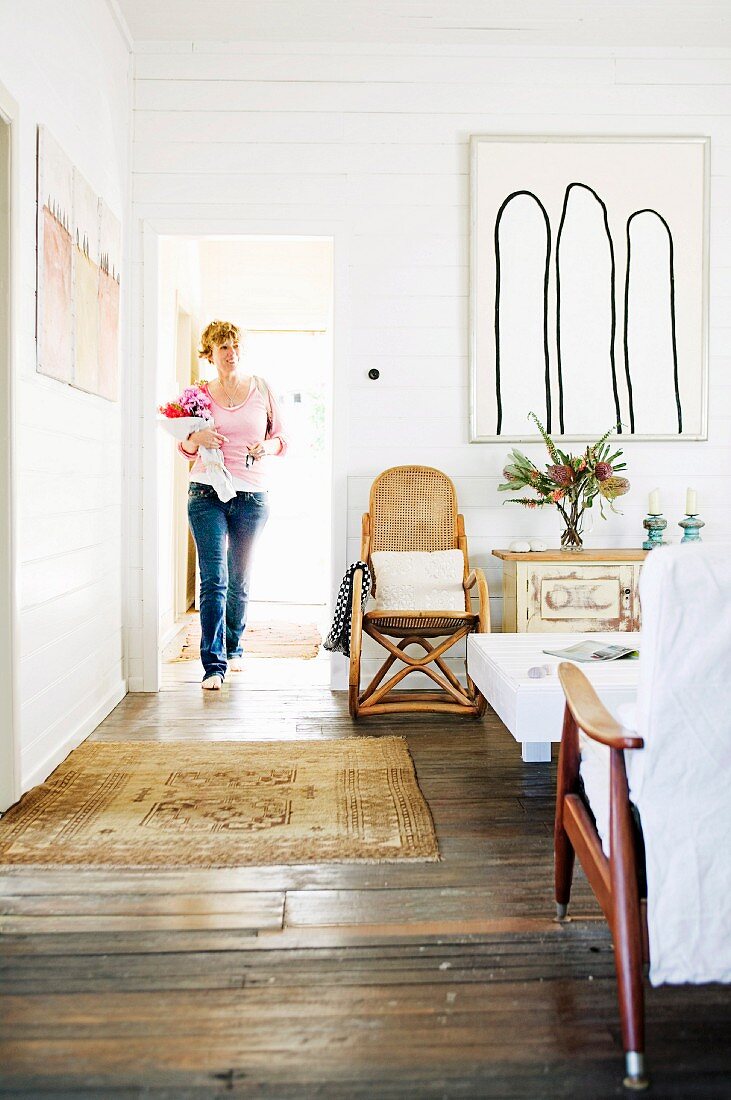 Frau in rustikalem Wohnzimmer mit Dielenboden; Rattansessel neben modernem Bild an weisser Holzwand