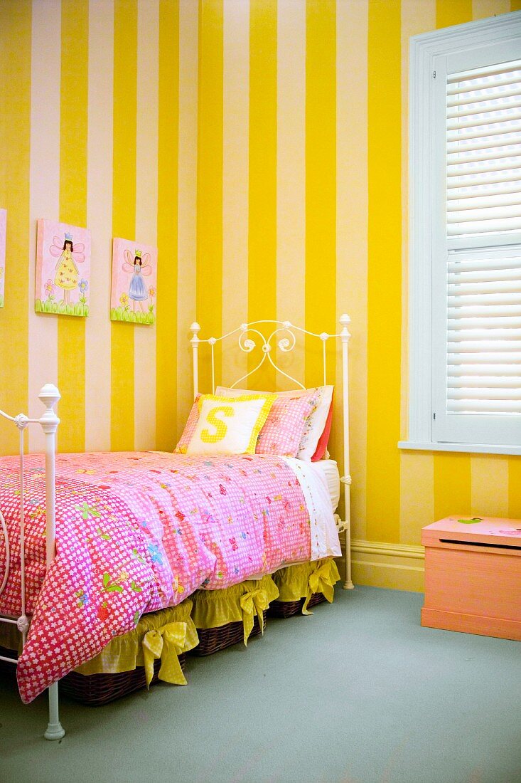Romantisches Mädchenzimmer - filigranes Metall Bettgestell und geblümte Bettwäsche vor gelbgestreifter Tapete an Wand