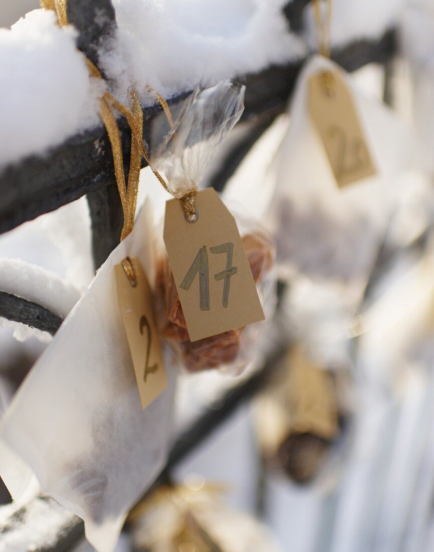 Kleine Tüten mit Plätzchen hängen als Adventskalender am verschneiten Zaun