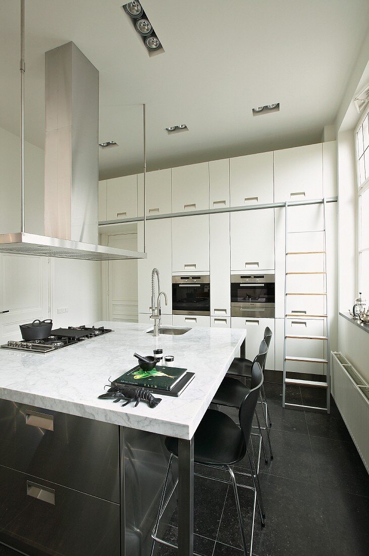 Kücheninsel mit Marmor-Arbeitsplatte in weisser Einbauküche mit schwarzen Bodenfliesen