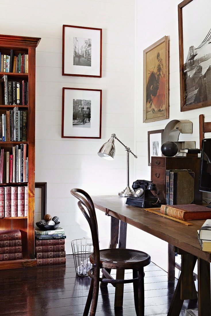 Thonetstuhl vor schlichtem Holztisch, Retro Chrom-Tischleuchte und Bücherschrank im Arbeitszimmer
