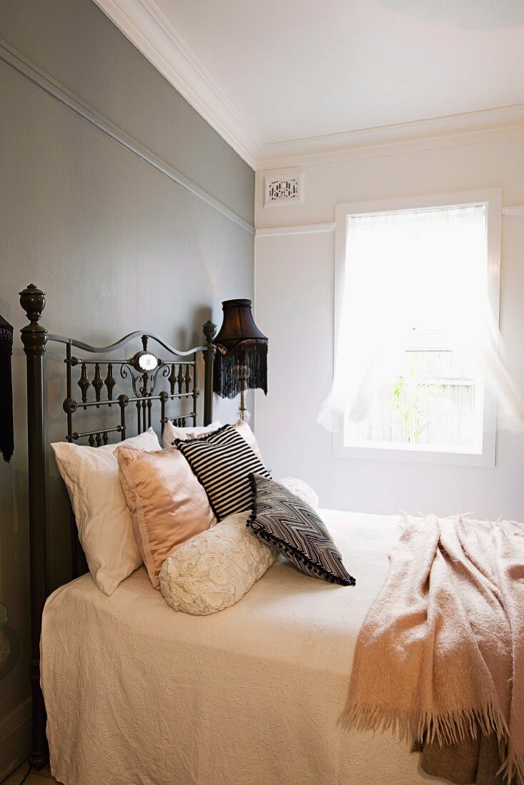 Französisches Bett mit antikem Metall Gestell vor grau getönter Wand in schlichtem Schlafzimmer mit nostalgischem Vintage-Flair