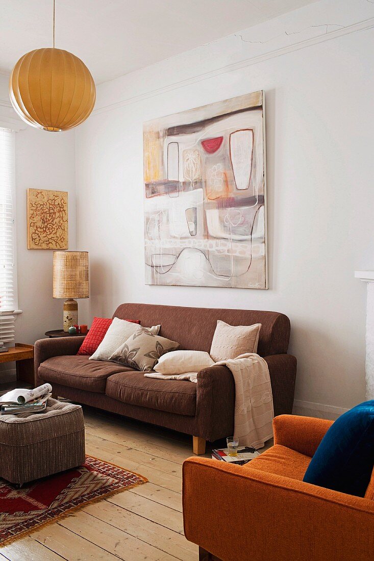 Erdtöne im Wohnzimmer, Retro Sofa vor Wand mit Bild und gemütlicher Polstersessel auf rustikalem Dielenboden