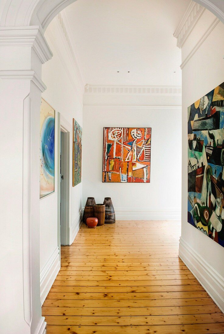 Spacious hallway in period building with wooden floor and modern artworks on walls with stucco elements