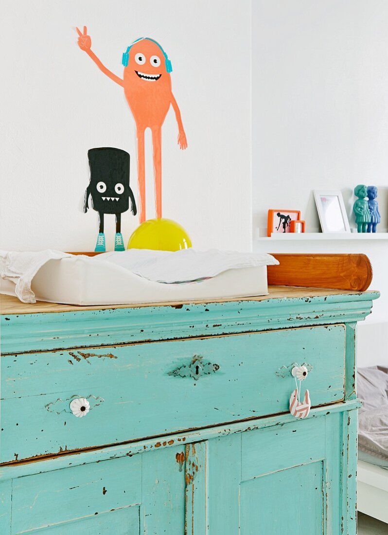 Rustic baby-changing cabinet with peeling turquoise paint and comic characters painted on wall