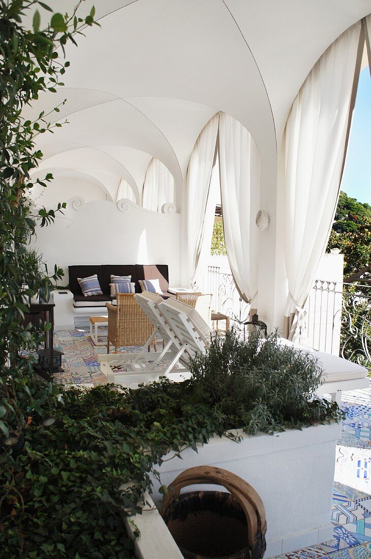 Seating area with loungers in cross-vaulted loggia with draped curtains and planted troughs