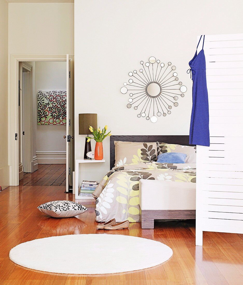 Round, white rug on parquet floor in modern bedroom; open door with view into hallway in background