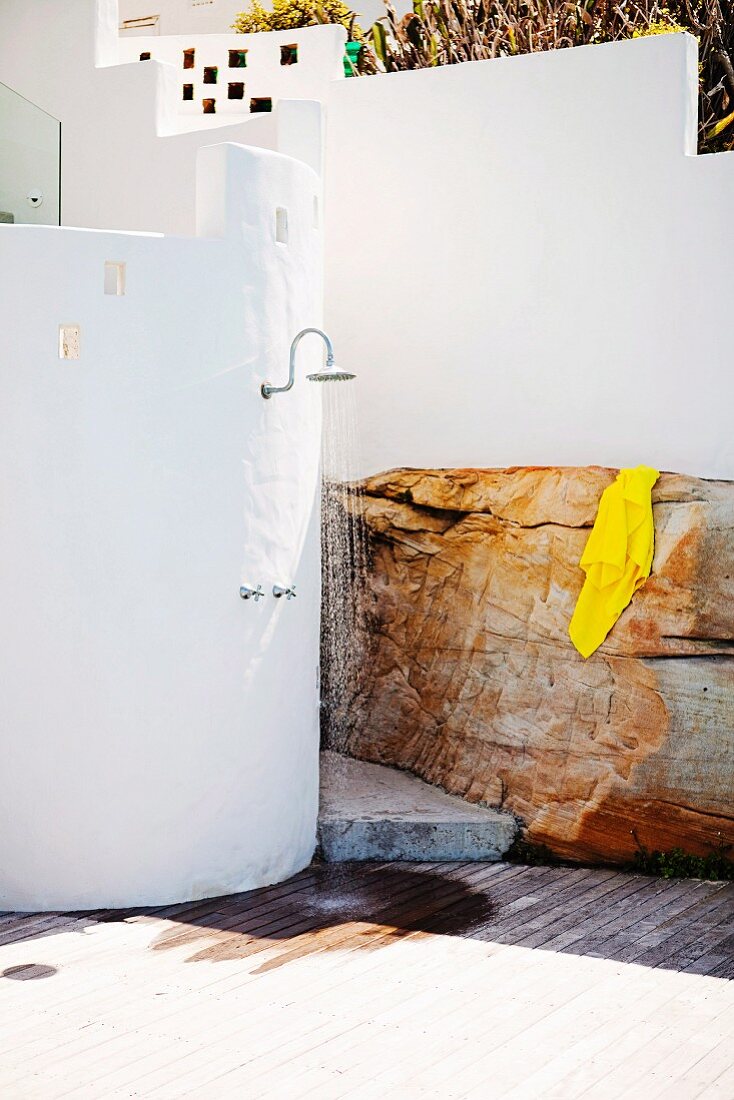 Outdoor shower on curved, white wall next to yellow towel on boulder